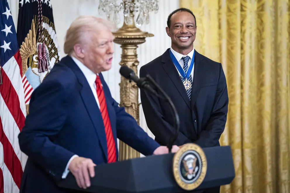 Donald Trump speaking as Tiger Woods looks at him with a smile during a reception honoring Black History Month in Washington, D.C., on February 20, 2025. | Source: Getty Images